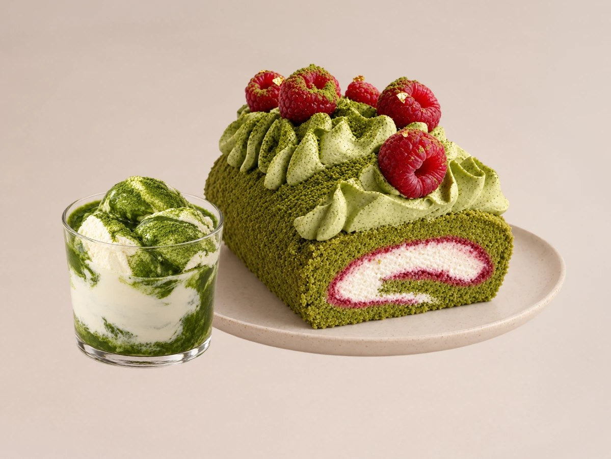 A matcha roll cake with raspberries beside a glass of matcha ice cream
