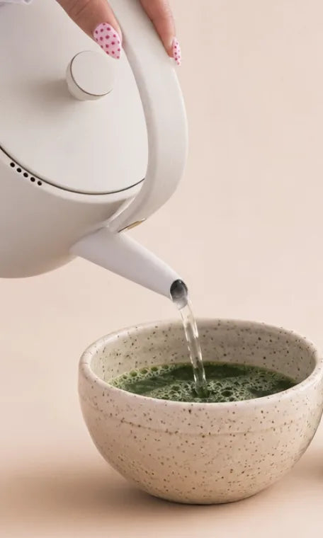 Water poured from a white kettle into a speckled bowl of matcha