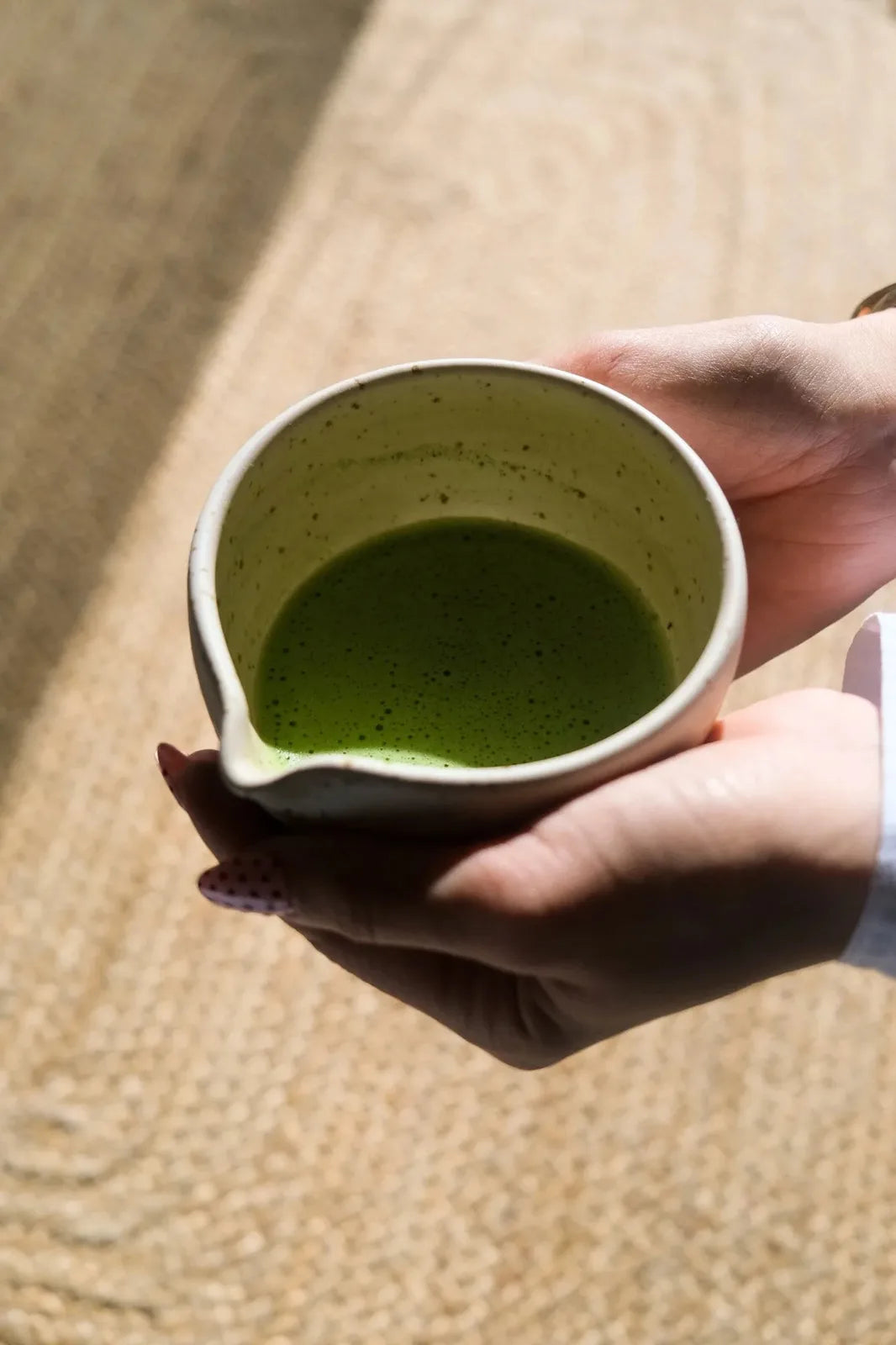 Hands holding a spouted bowl of whisked matcha