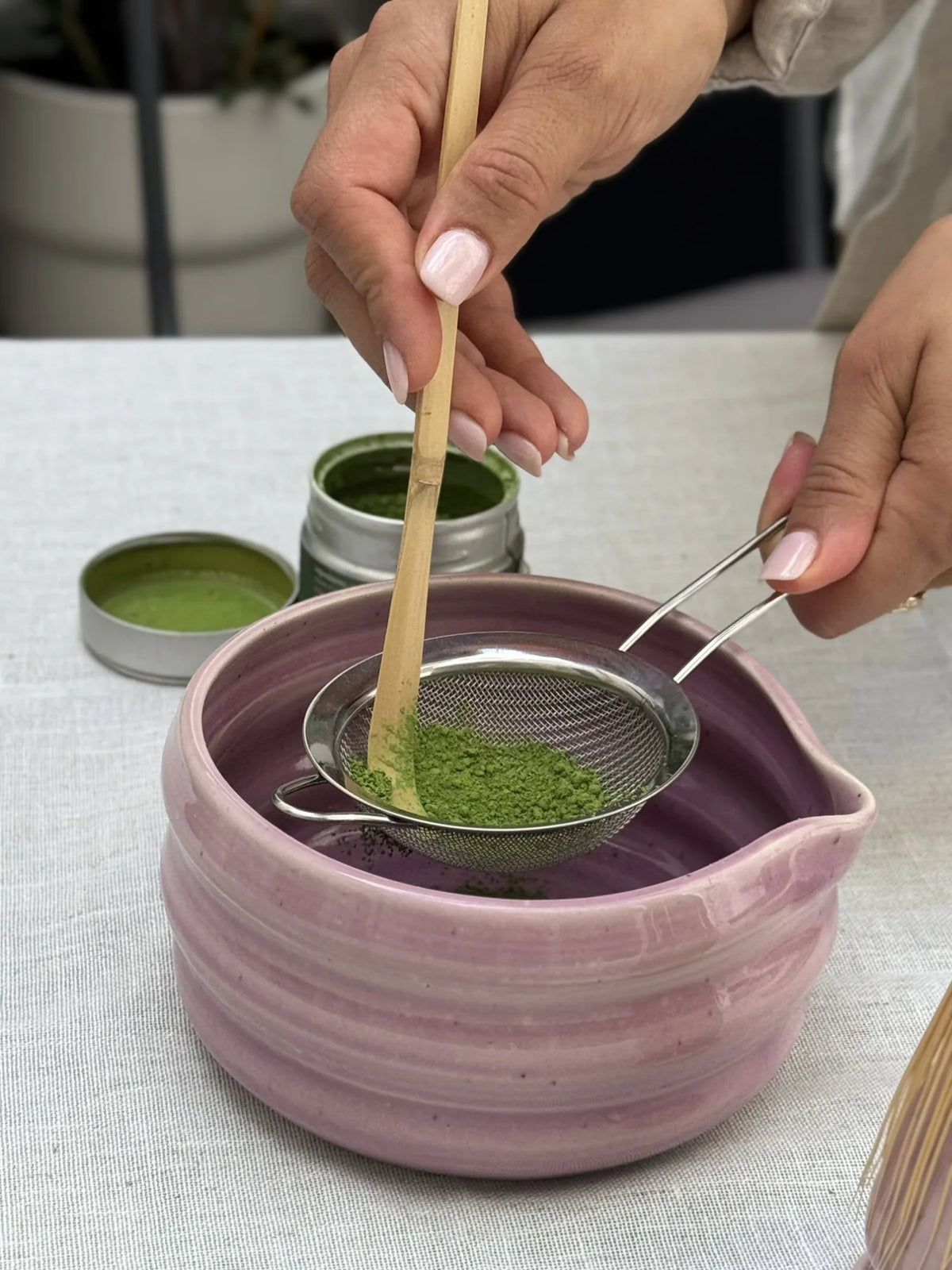 Sifting matcha into a pink bowl, open tin without label in view